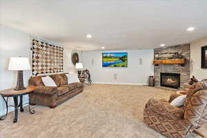 Living room with light carpet, a stone fireplace, a textured ceiling, and baseboards