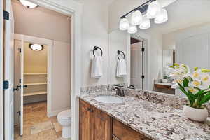 Bathroom featuring stone tile floors, baseboards, toilet, a walk in closet, and vanity