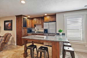 Kitchen featuring stainless steel fridge with ice dispenser, dark stone countertops, black microwave, a peninsula, and a kitchen breakfast bar