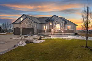 French provincial home featuring driveway, a front lawn, an attached garage, and stone siding