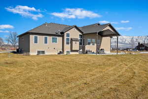 Back of house featuring a shingled roof, a lawn, a mountain view, central AC, and stucco siding