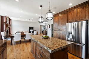 Kitchen featuring light wood-style floors, open floor plan, stainless steel fridge with ice dispenser, a center island, and decorative light fixtures