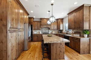 Kitchen featuring appliances with stainless steel finishes, decorative light fixtures, a center island, light stone countertops, and light wood-type flooring