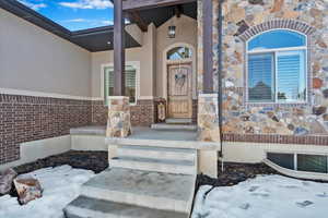 Snow covered property entrance with stone siding, visible vents, and stucco siding