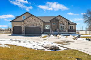 View of front of property featuring a garage, concrete driveway, stone siding, and stucco siding