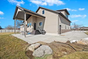 Back of house with brick siding, a yard, a patio, stucco siding, and fence