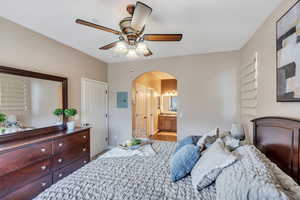 Bedroom with arched walkways, ceiling fan, connected bathroom,  and light wood-style flooring