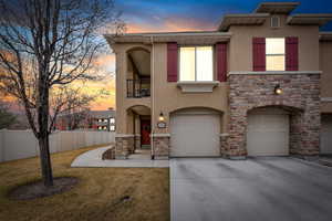 View of front of property featuring driveway, garage, stone/stucco siding, and fence