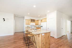 Kitchen featuring a sink, a breakfast bar, light wood-type flooring, white appliances, and a kitchen island with sink