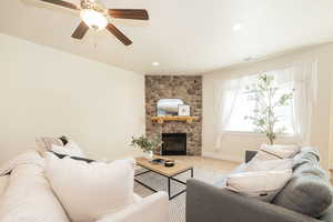 Living room featuring recessed lighting, visible vents, ceiling fan, a stone fireplace, and baseboards