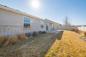 Back of property with brick siding, stucco siding, a fenced backyard, a yard, and a patio