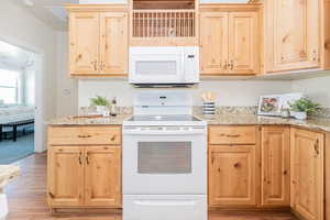 Kitchen with white appliances, light stone countertops, light wood-type flooring, and light brown cabinetry