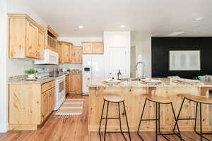 Kitchen with a kitchen bar, white appliances, light wood-style floors, and light brown cabinetry