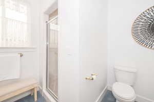 Bathroom featuring a stall shower, baseboards, and toilet