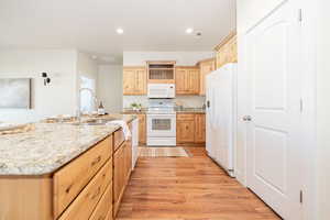 Kitchen with light wood-style flooring, light brown cabinets, a sink, recessed lighting, and white appliances