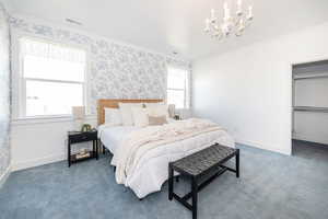 Carpeted bedroom with visible vents, wallpapered walls, baseboards, ornamental molding, and an inviting chandelier