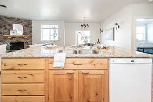 Kitchen featuring open floor plan, light stone counters, white dishwasher, and a sink