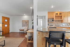 Kitchen with crown molding, dark wood finished floors, stainless steel microwave, decorative backsplash, and light brown cabinetry