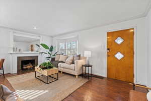 Living room featuring crown molding, a tiled fireplace, baseboards, and wood finished floors