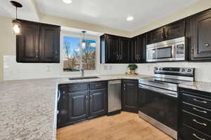 Kitchen with light wood-style flooring, light stone counters, stainless steel appliances, pendant lighting, and a sink