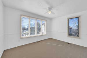 Carpeted empty room with baseboards, visible vents, and a ceiling fan