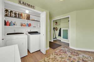 Clothes washing area featuring laundry area, light wood finished floors, washing machine and dryer, and baseboards