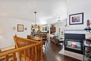 Dining space featuring dark wood-style floors, a tile fireplace, vaulted ceiling, and ceiling fan with notable chandelier