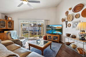 Living area with lofted ceiling, dark wood-style floors, a ceiling fan, and baseboards