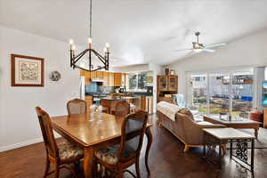 Dining space with lofted ceiling, dark wood-style floors, baseboards, and ceiling fan with notable chandelier