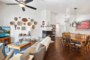 Living area with baseboards, dark wood finished floors, a fireplace, high vaulted ceiling, and ceiling fan with notable chandelier