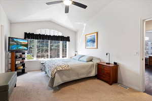 Carpeted bedroom featuring lofted ceiling, ceiling fan, visible vents, and baseboards