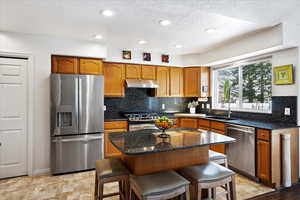 Kitchen with a center island, appliances with stainless steel finishes, a sink, under cabinet range hood, and a kitchen breakfast bar