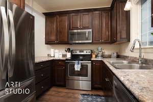 Kitchen with dark wood-style floors, stainless steel appliances, a sink, and dark brown cabinetry