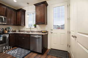 Kitchen featuring dark countertops, dark wood-style flooring, decorative light fixtures, stainless steel appliances, and a sink