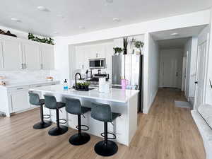 Kitchen featuring light wood-type flooring, tasteful backsplash, appliances with stainless steel finishes, and a kitchen breakfast bar