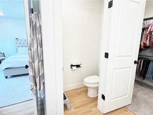 Ensuite bathroom with baseboards, toilet, ensuite bath, wood finished floors, and a spacious closet