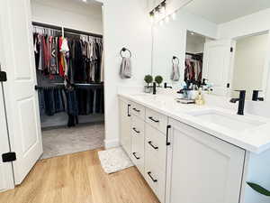 Bathroom with double vanity, a walk in closet, a sink, and wood finished floors