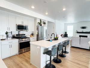 Kitchen featuring stainless steel appliances, light wood-type flooring, a sink, and a kitchen bar