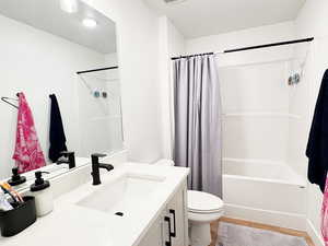 Full bath featuring toilet, wood finished floors, visible vents, vanity, and shower / bathtub combination with curtain