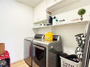 Clothes washing area featuring light wood-type flooring, washing machine and dryer, cabinet space, and baseboards