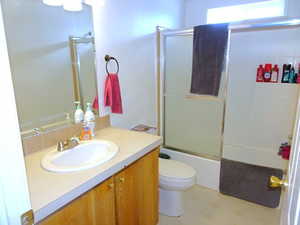 Bathroom with toilet, combined bath / shower with glass door, and vanity