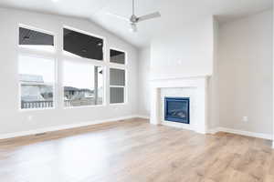 Unfurnished living room featuring baseboards, visible vents, a ceiling fan, a glass covered fireplace, and light wood-style flooring