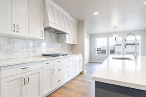 Kitchen featuring stainless steel gas cooktop, premium range hood, a sink, white cabinets, and decorative light fixtures