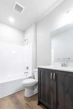 Bathroom with shower / bathtub combination, toilet, wood finished floors, vanity, and visible vents