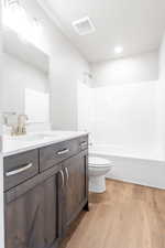 Full bathroom with bathtub / shower combination, visible vents, toilet, vanity, and wood finished floors