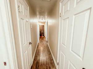 Corridor featuring baseboards, a textured ceiling, and wood finished floors