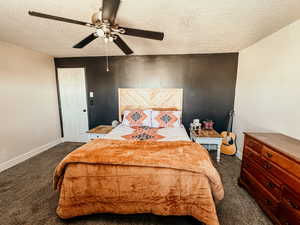 Carpeted bedroom with a textured ceiling, baseboards, and a ceiling fan