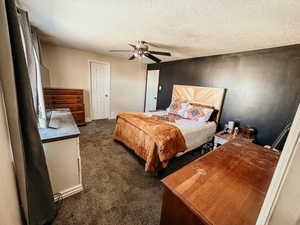 Bedroom with a ceiling fan, baseboards, dark carpet, and a textured ceiling