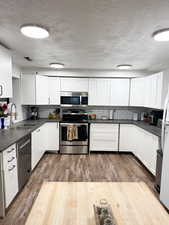 Kitchen with appliances with stainless steel finishes, dark countertops, a sink, and white cabinets