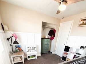 Bedroom featuring ceiling fan, wainscoting, and dark carpet